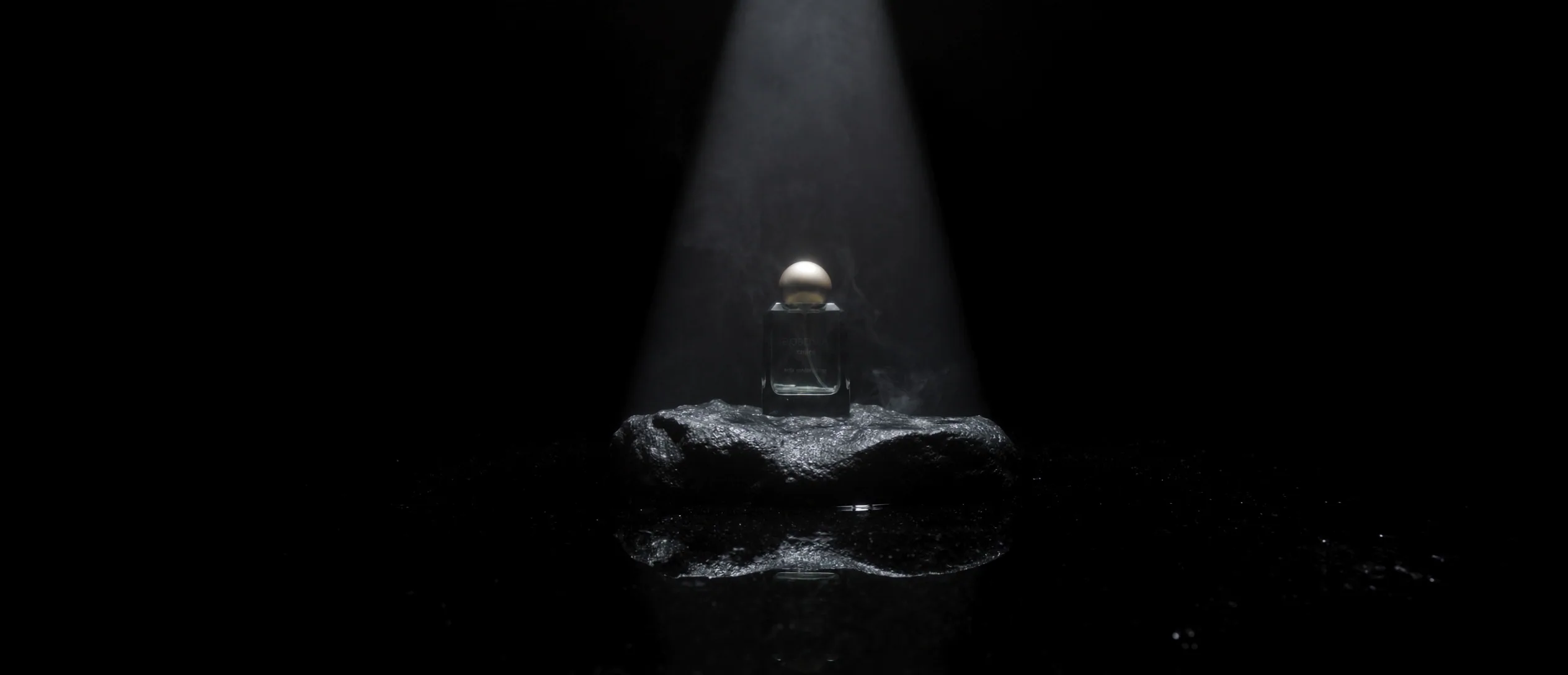 Flacon de parfum sur une pierre noire traversé par un faisceau de lumière