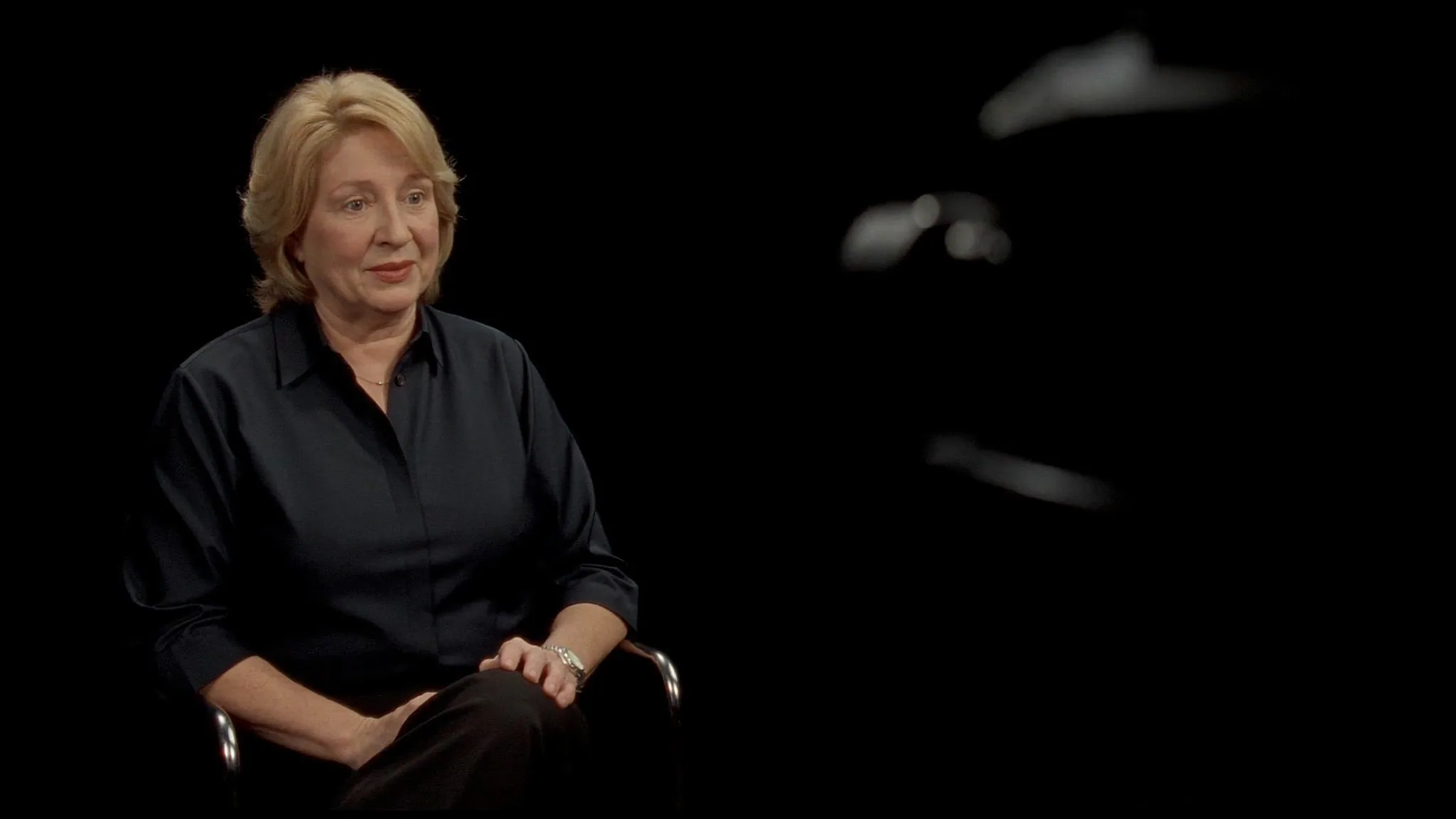 Femme dirigeante interviewée dans un studio sombre, caméra floue au premier plan